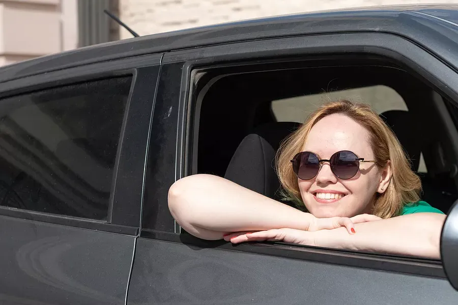 Girl sitting in her car, wearing sunglasses and smiling