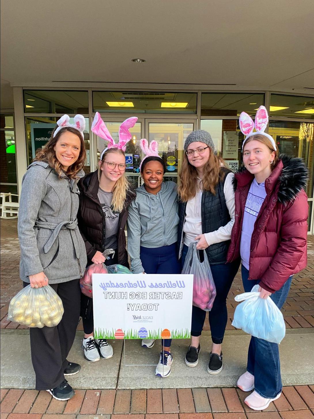 Students participating in Easter Egg Hunt, wearing bunny ears and holding bags of eggs.
